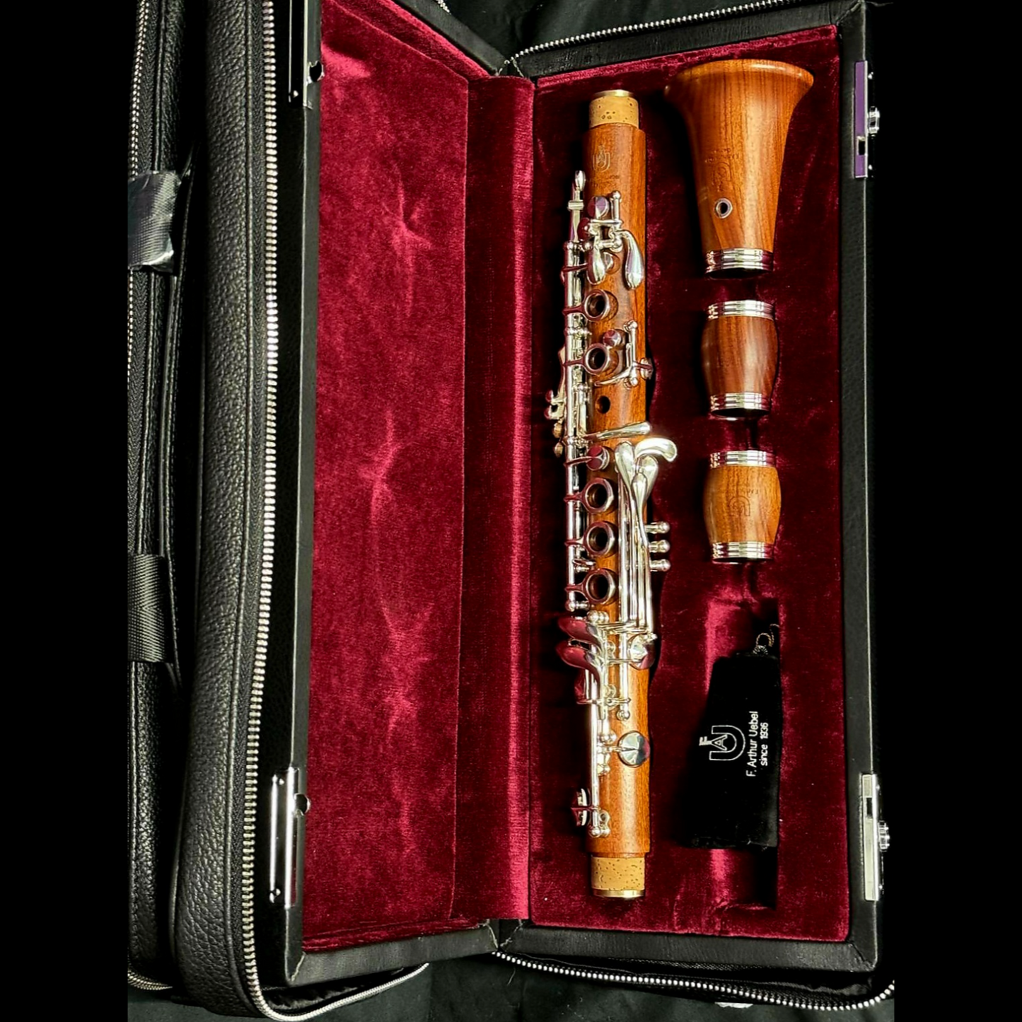 Uebel Superior Eb clarinet in mopane wood, laying disassembled in its case, which is laying open to show how the instrument pieces are arranged inside.. Case lining is a bold red, which highlights the red color of the wood. 