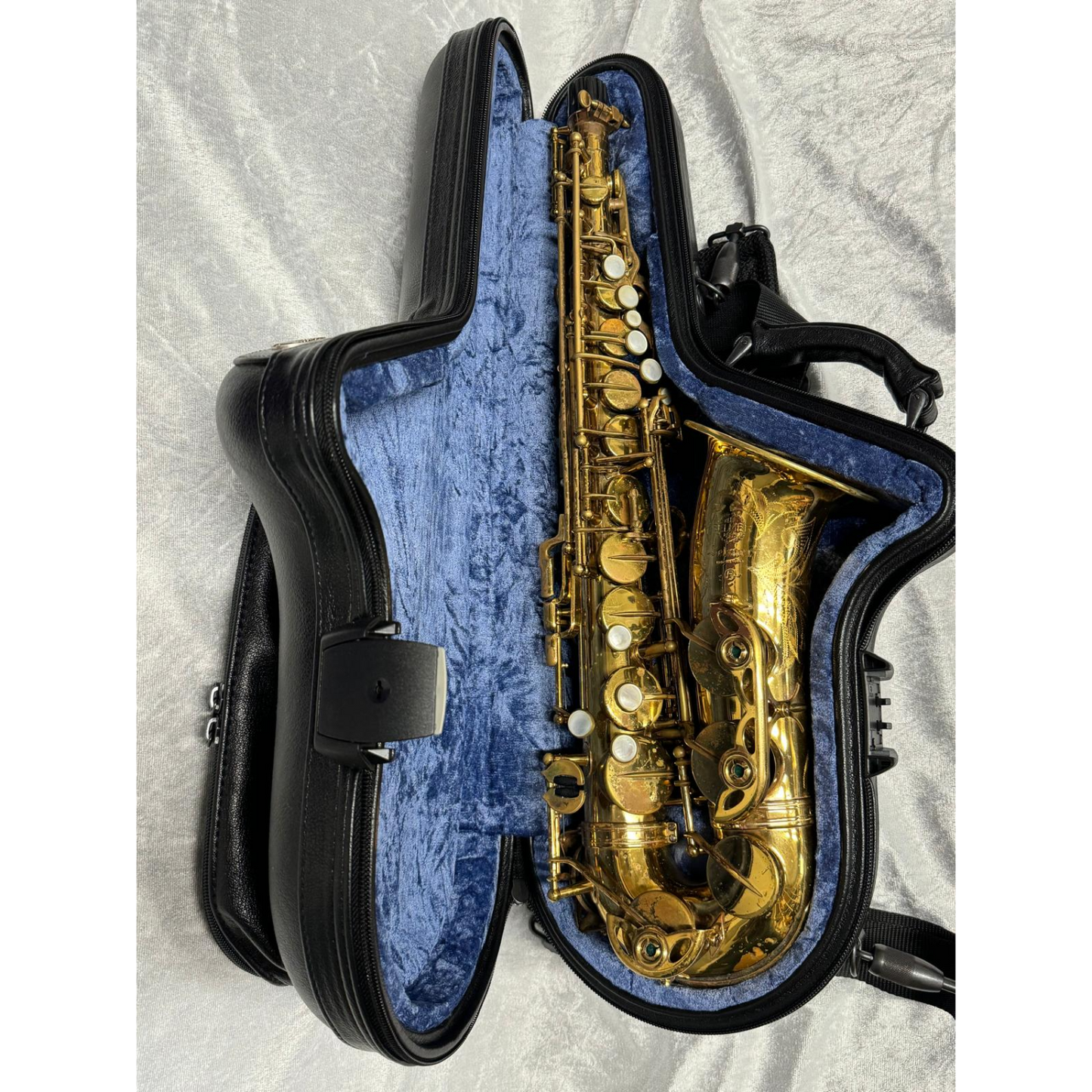 black leather case laying open with saxophone inside, blue interior, on white velvet background