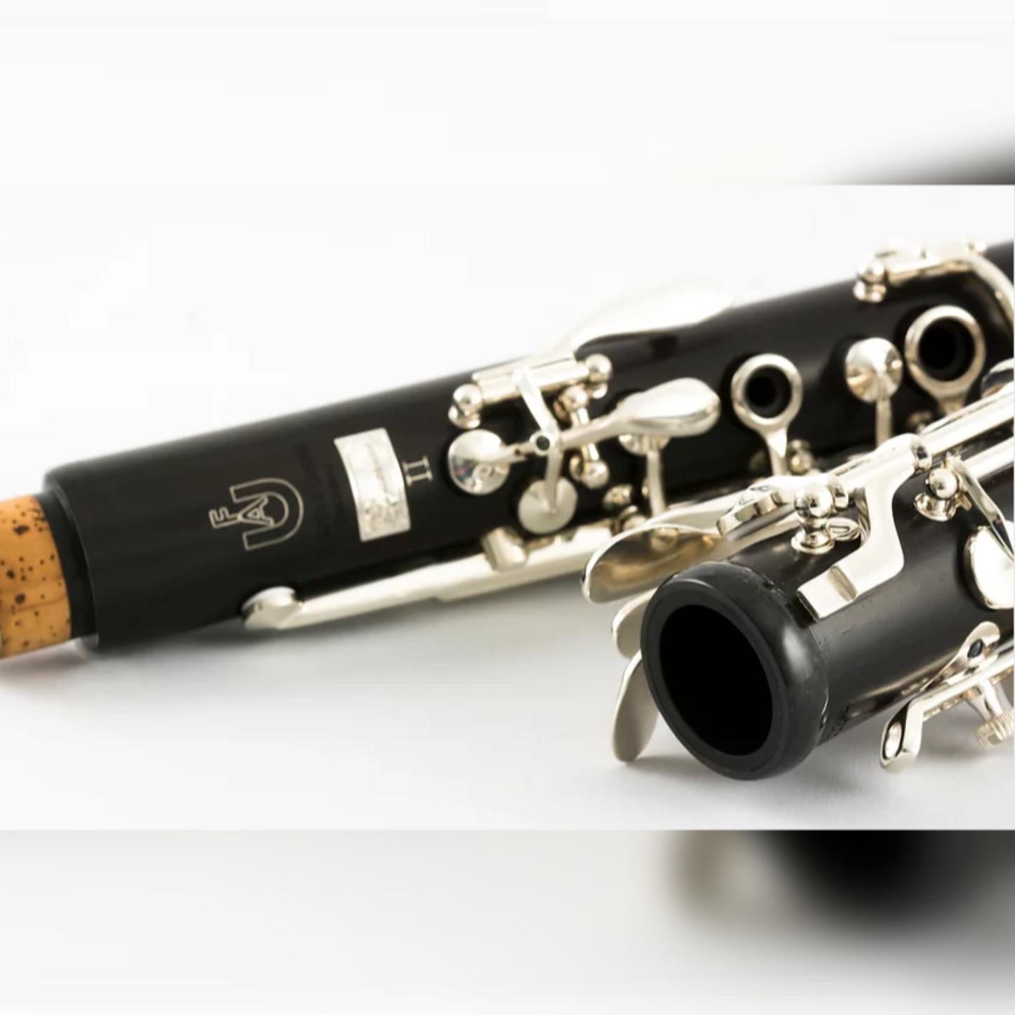 Disassembled Uebel Superior II Bb clarinet on a white surface, with a closeup on the carbon fiber center joint ring and the Superior II logo in the background