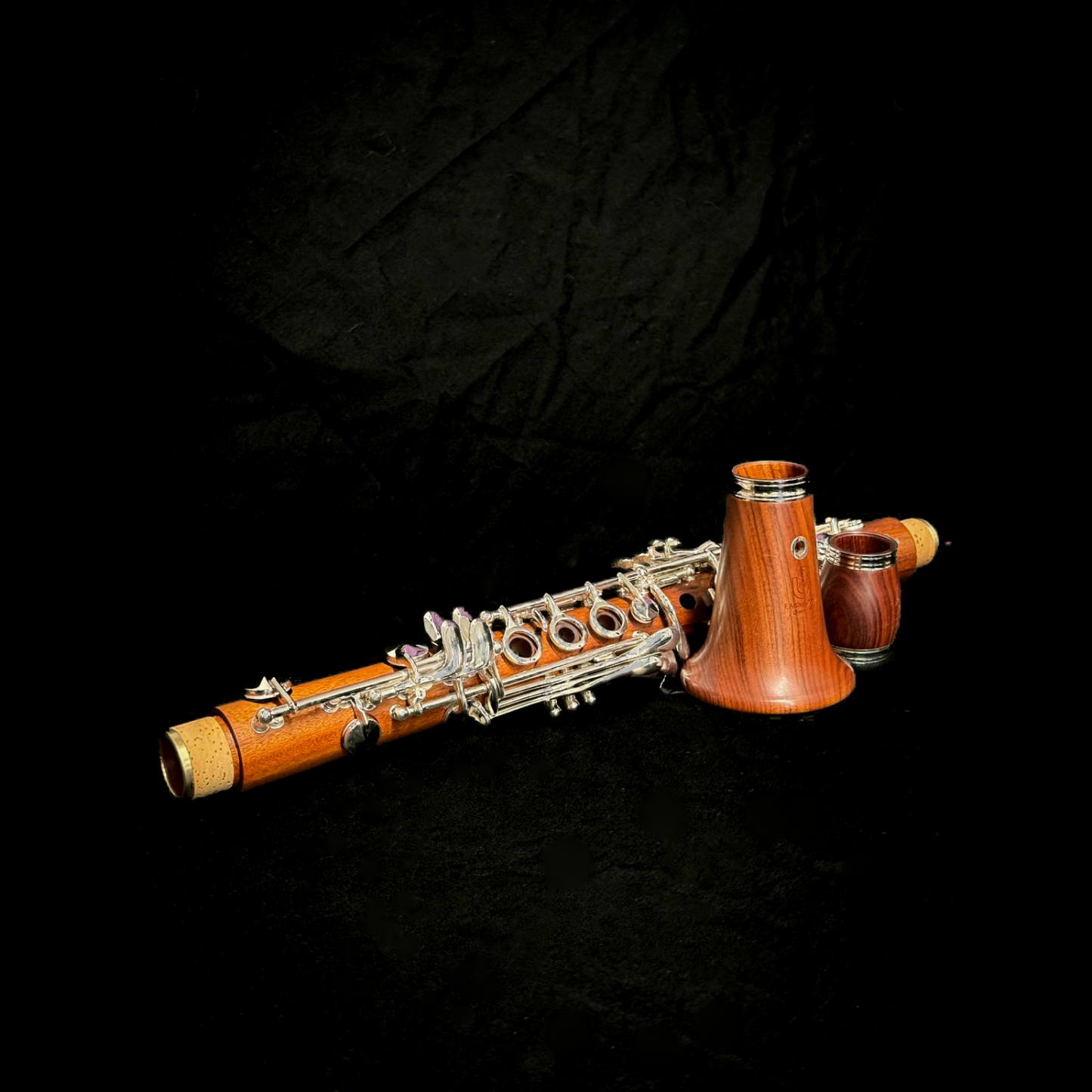 Uebel Superior Mopane Eb clarinet, disassembled against a dramatic black fabric background, highlighting the gorgeous orange-red color and flame-like grain of the wood