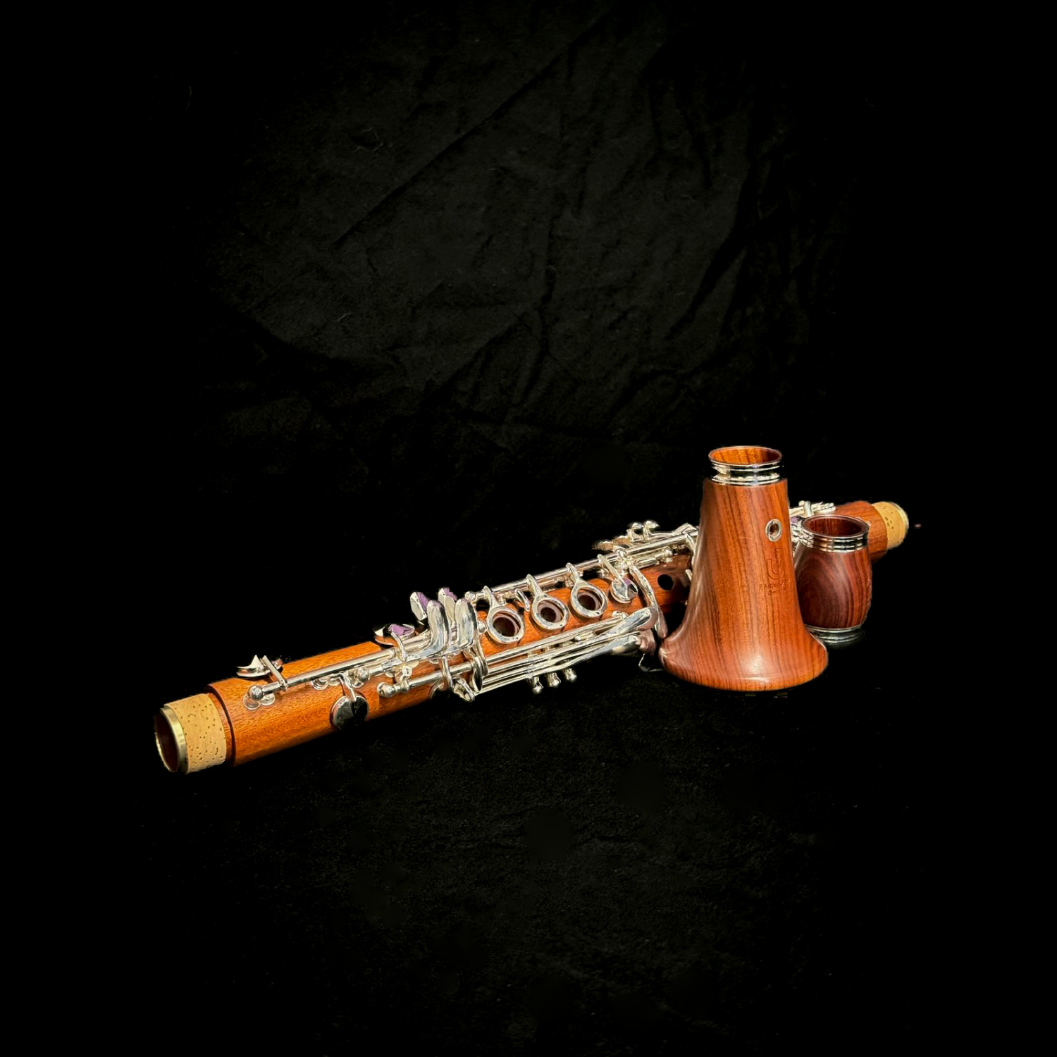 Uebel Superior Mopane Eb clarinet, disassembled against a dramatic black fabric background, highlighting the gorgeous orange-red color and flame-like grain of the wood